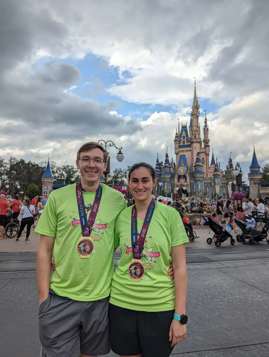 Danielle and Quentin at Disney with their half marathon medals in front of Cinderella's Castle